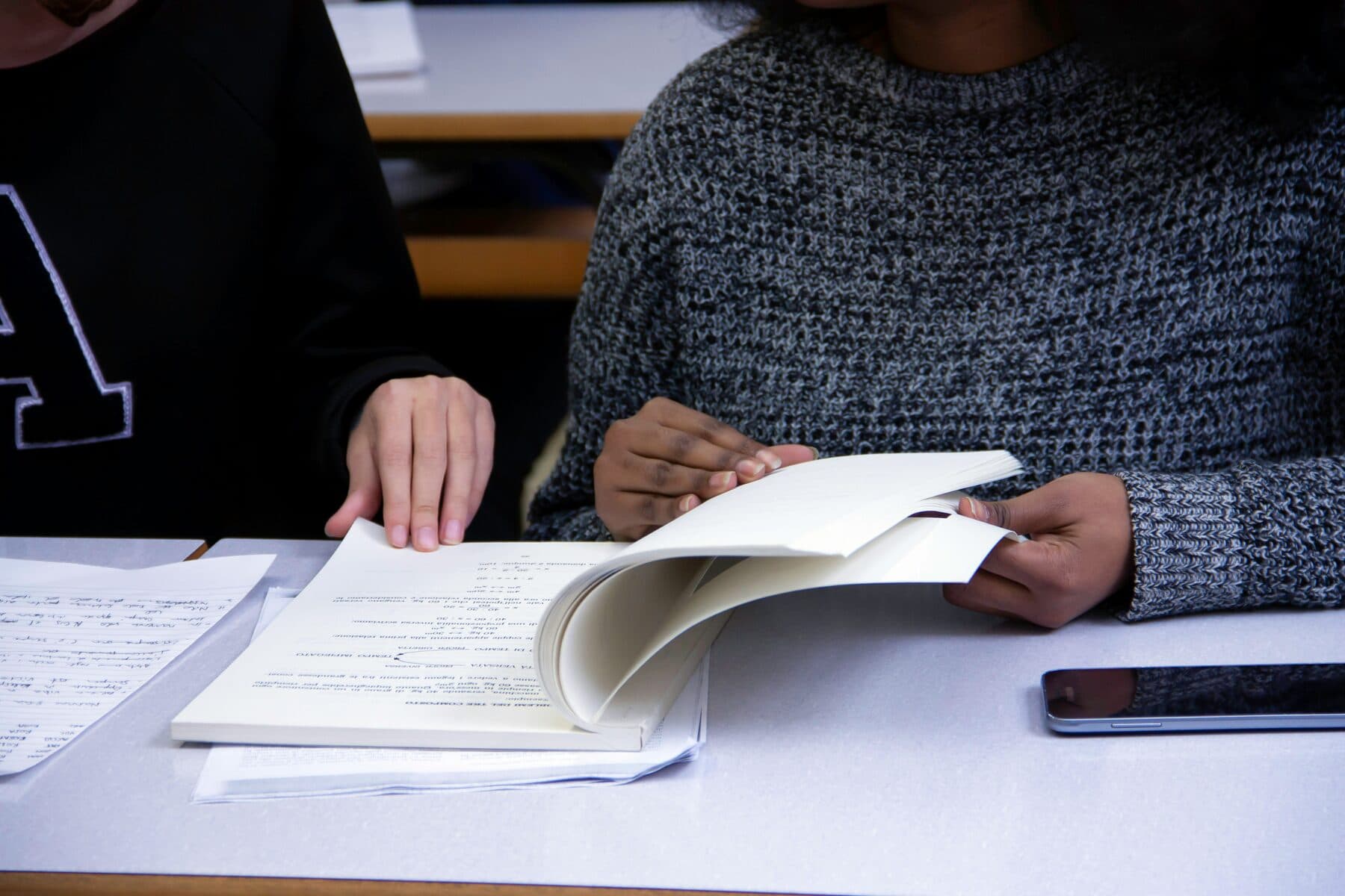 Two students working through written coursework at a desk.
